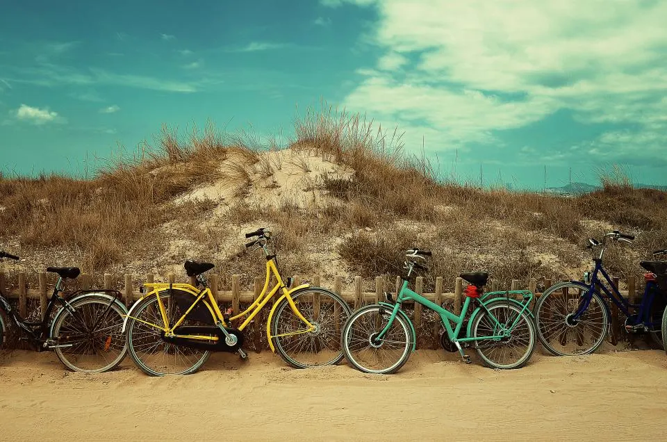 Four city bikes leaning on a fence in front of a sand dune