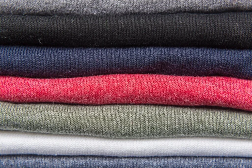 A stack of folded T-shirts in grey, navy, red and green