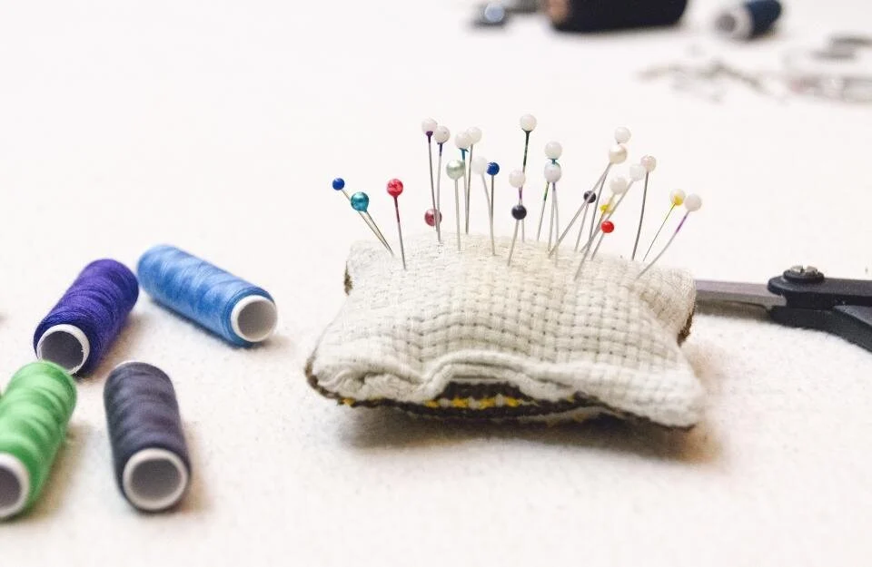A pin cushion with coloured pins and reels of thread on a white table