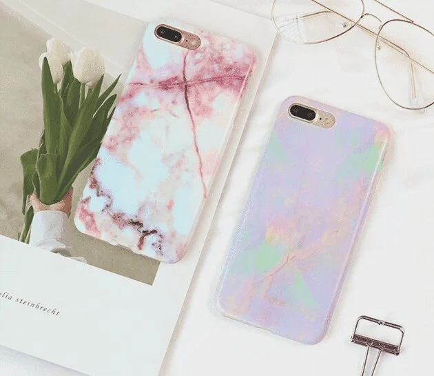 Two marble-print phone cases on a white desk with tulips and glasses