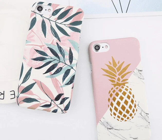 A leaf-print case and a pineapple-print case on a white desk