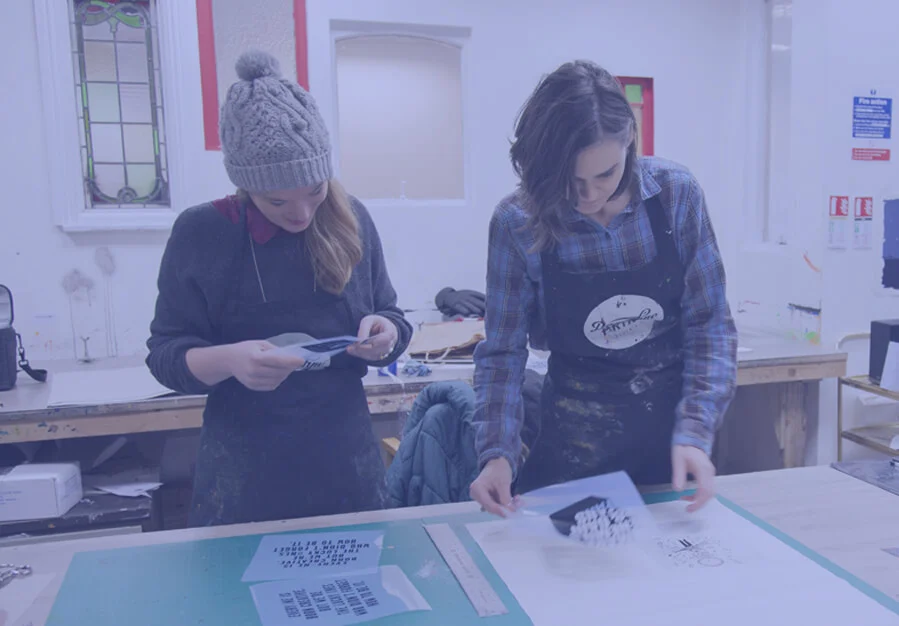 Two printers checking screen-printed sheets at a workshop table