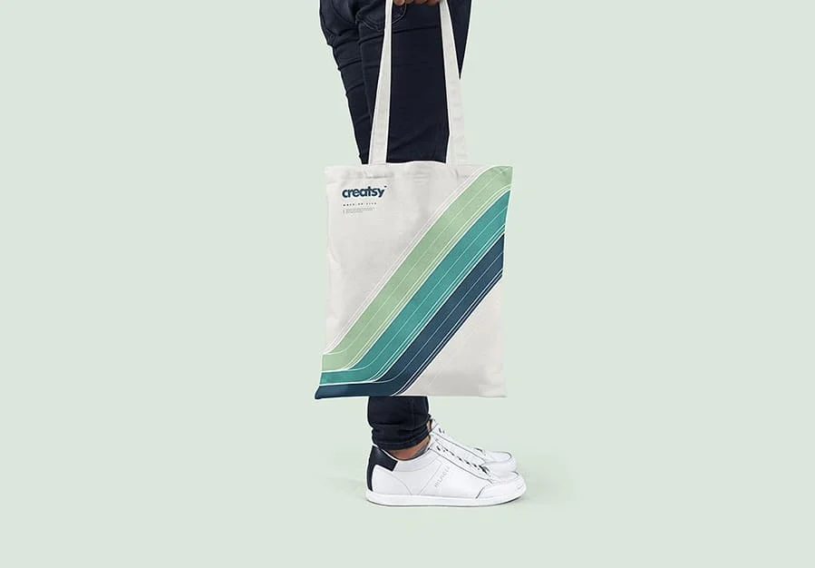 A person in jeans and white sneakers carrying a white tote bag with green stripes