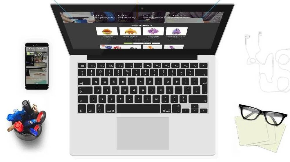 A laptop with the online store open, a phone, pens, glasses and notes on a white desk